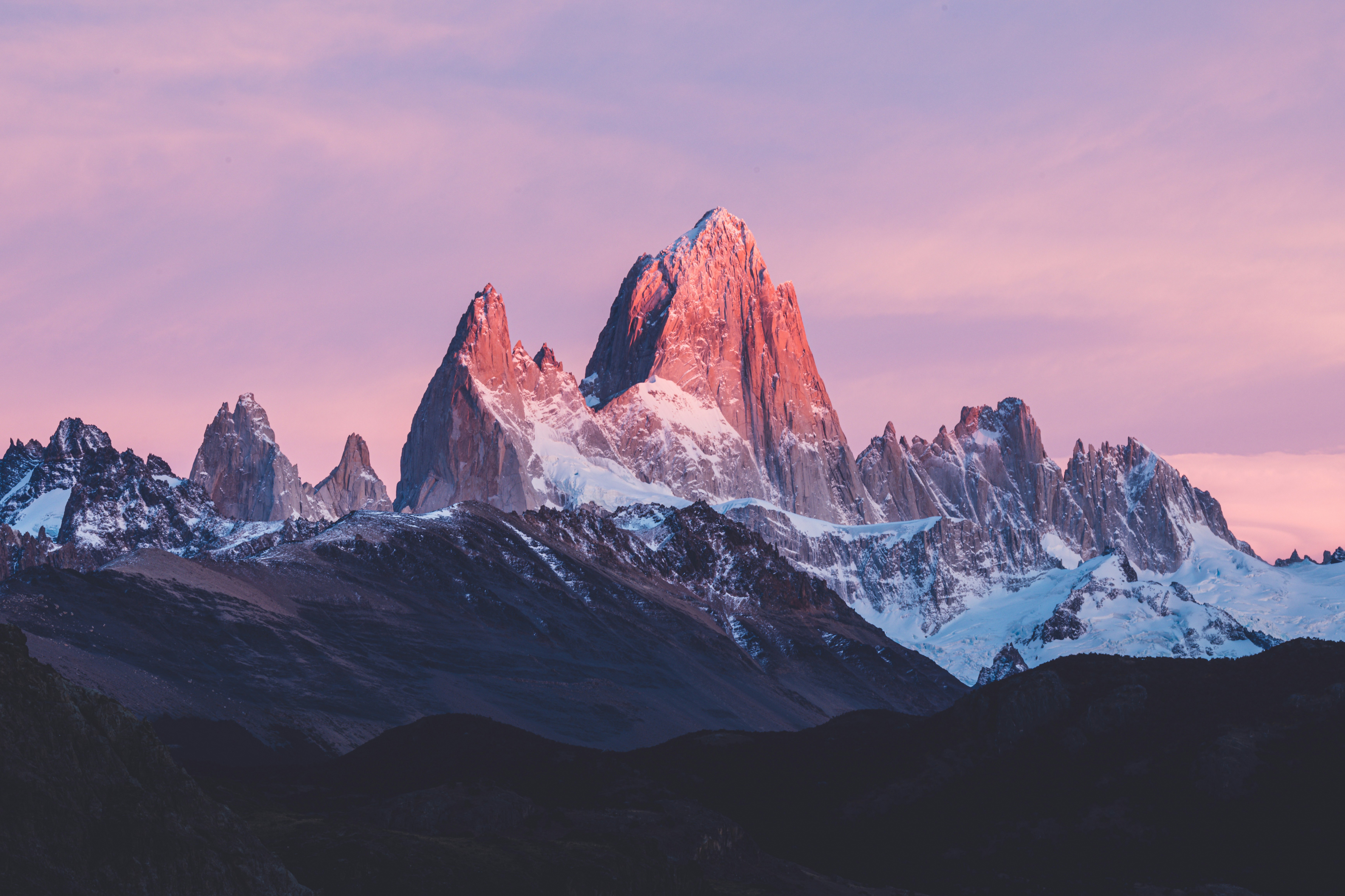 Silhouette of a solo backpacker watching the orange sunrise hitting the jagged peaks of Mount Fitz Roy in Patagonia
