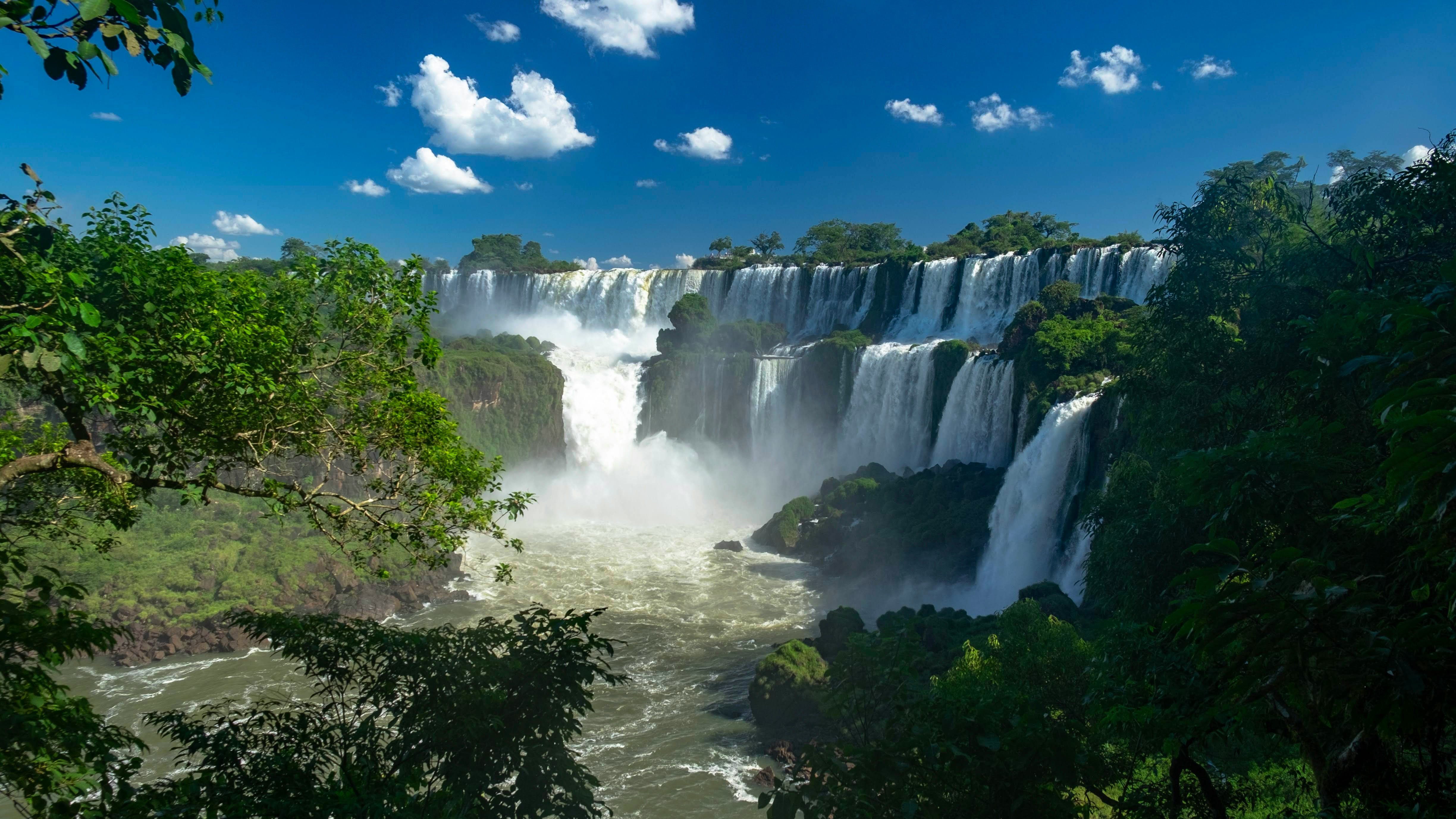 Massive Iguazu waterfalls cascading into a misty jungle gorge with a rainbow forming in the spray